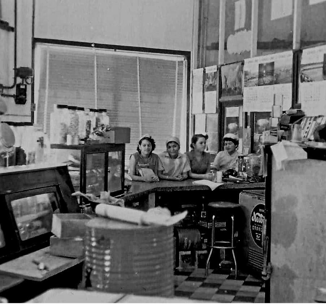 Black-and-white archival photograph of four people behind a soda-fountain counter